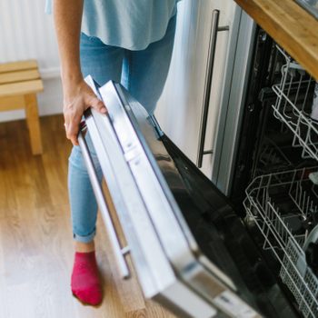 anonymous woman standing in a kitchen opening the dishwasher