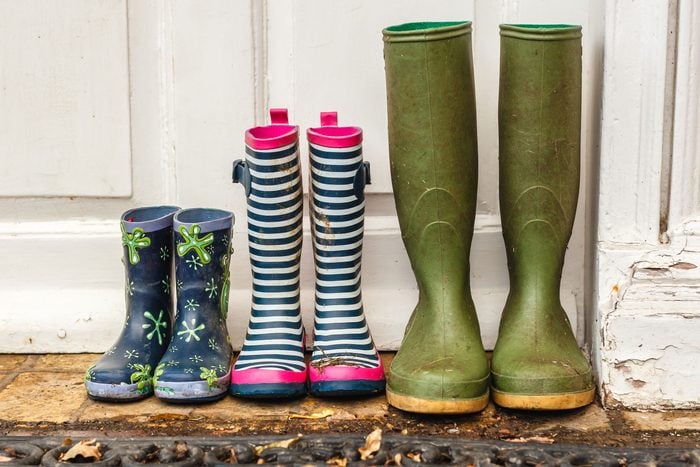 three pairs of dirty rainboots lined up outside a door