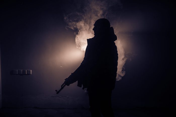 Silhouette of man with assault rifle ready to attack on dark toned foggy background or dangerous bandit holding gun in hand. Shooting terrorist with weapon theme decor
