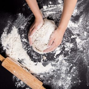 Baking preparing background. Female hands knead dough on the worktop.