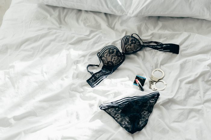 black lace lingerie near condom, handcuffs and condom on bed 