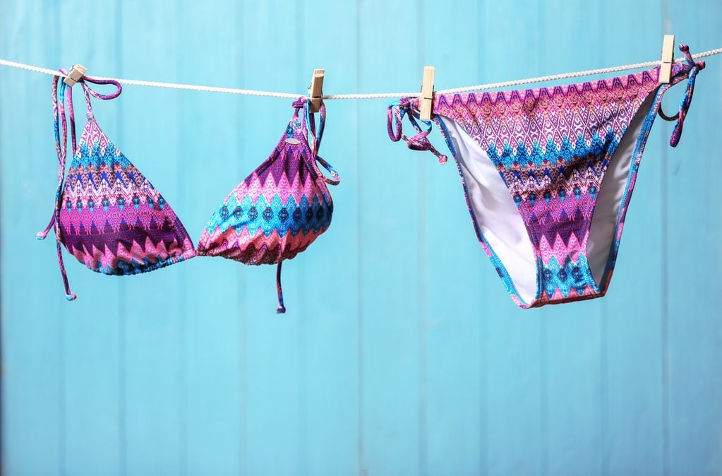 Stylish bikini hanging on rope against color background