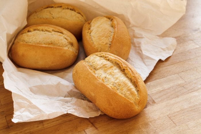 bread rolls or buns for breakfast fresh from the bakery in a white paper bag on a wooden table, selected focus, narrow depth of field