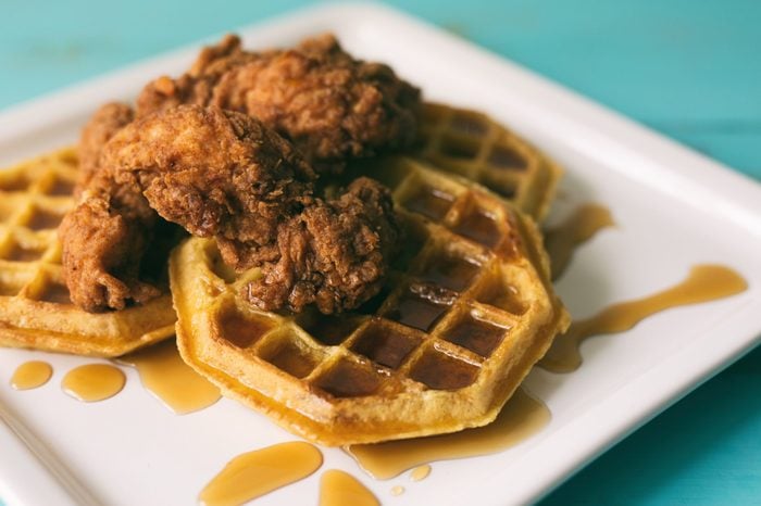 Chicken and waffles with syrup on a white square plate. 