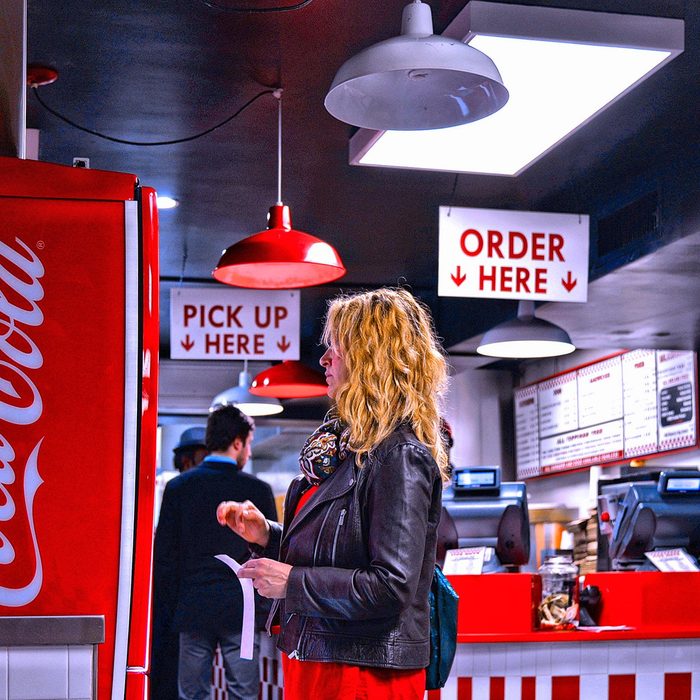 People eating in Five Guys burger fast food restaurant and girl taking a Coca Cola drink