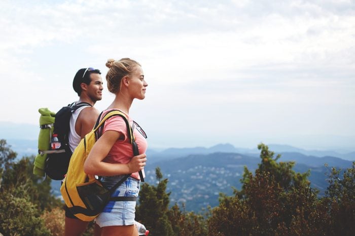 Young man and woman travelers are enjoying amazing nature view during their backpacking, two hikers with rucksacks are resting after active walking in mountains during their summer weekend overseas