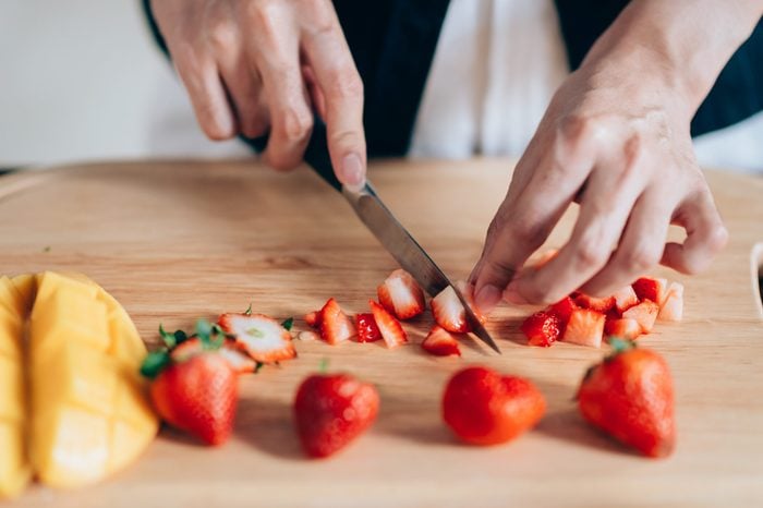 Chef Hand and Knife Slicing Fresh strawberry on wooden cutting board.