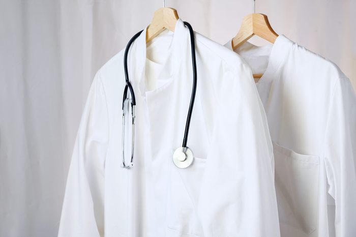 white medical doctor or physician lab coats with stethoscope hanging on clothes hangers, copy space, selected focus