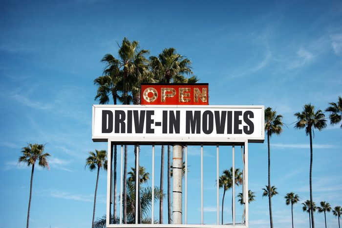 aged and worn vintage photo of old drive in movie sign with palm trees