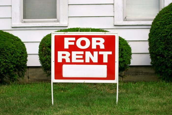FOR RENT sign with house behind it, copy space on sign
