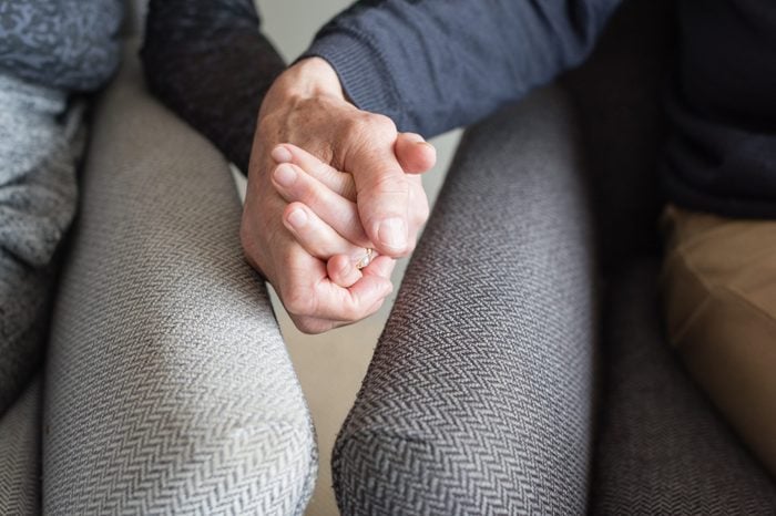 Close up of older couple in armchairs holding hands (cropped and selective focus)
