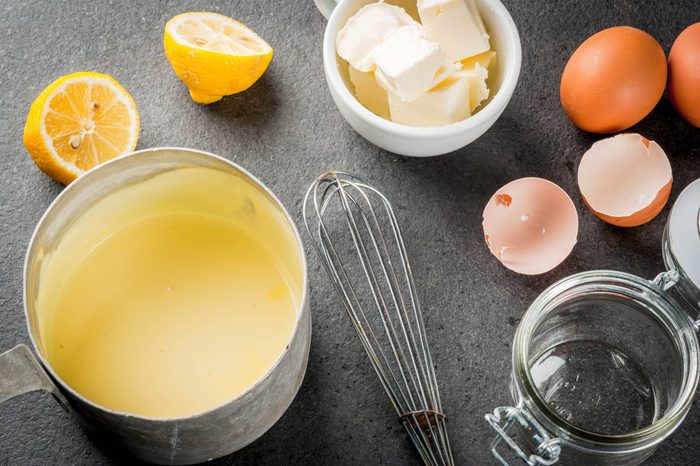 Traditional basic sauces. French cuisine. Hollandaise sauce in a metal saucepan, with ingredients for cooking - eggs, butter, lemons. On a black stone table. Copy space top view
