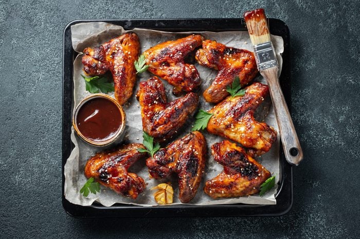 Roasted chicken wings in barbecue sauce with sesame seeds and parsley in a baking tray on a dark table. Top view. Tasty snack for beer on a dark background. Flat lay.