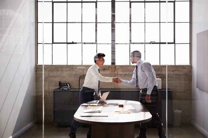 Two businessmen stand shaking hands in an office, side view
