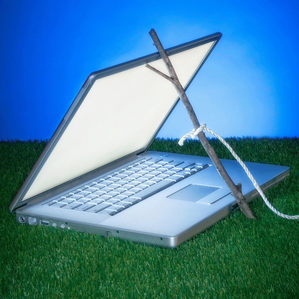 a laptop in the grass held open with a stick trap. alert icons appearing.