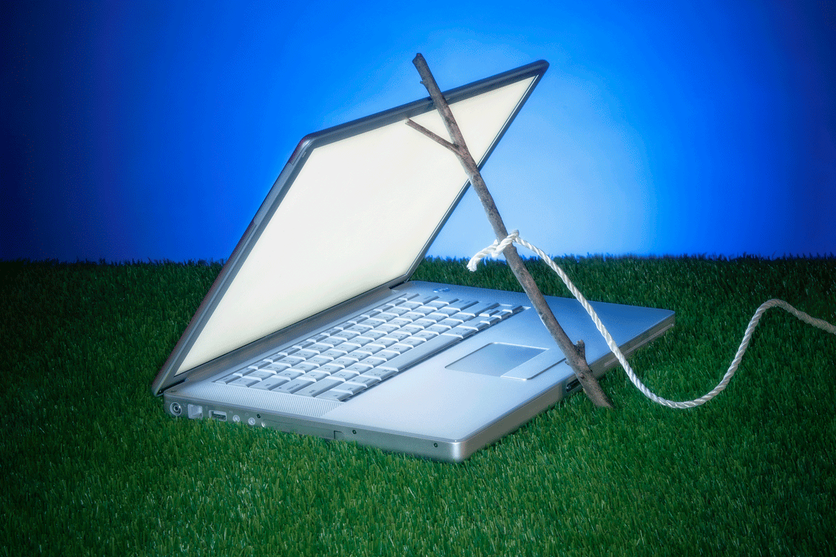 a laptop in the grass held open with a stick trap. alert icons appearing.
