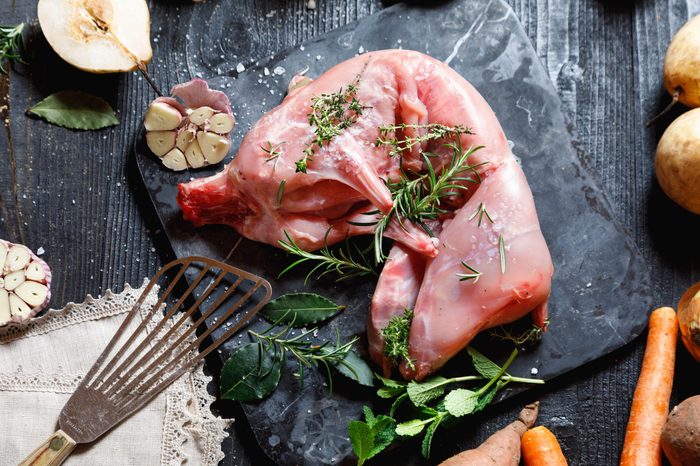 Whole Forest wild rabbit, Recipe with apple pie, Raw meat with spices and vegetables, Sea salt, red, white pepper and coriander in clay pots on an old black rustic table. magazine cover, copy space