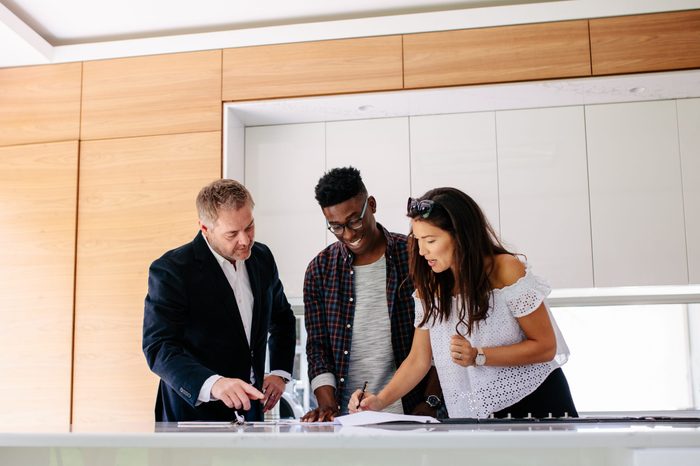 Couple signing a contract documents while standing inside a house with real estate agent. Interracial couple with realtor signing mortgage contract.