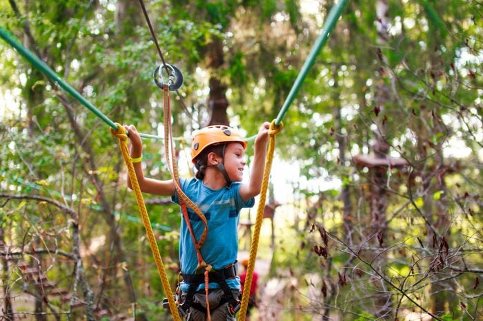 boy passes a rope obstacle course in the forest. cheerful child bravely overcomes extreme rope route outdoors. zip line