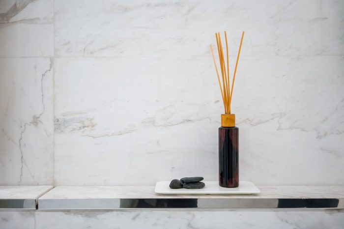 Scented diffuser stick in black glass bottle against white marble wall background for decoration in luxury bathroom.