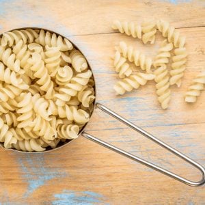 healthy, gluten free quinoa pasta (fusilli) - top view of a metal measuring cup against painted wood;