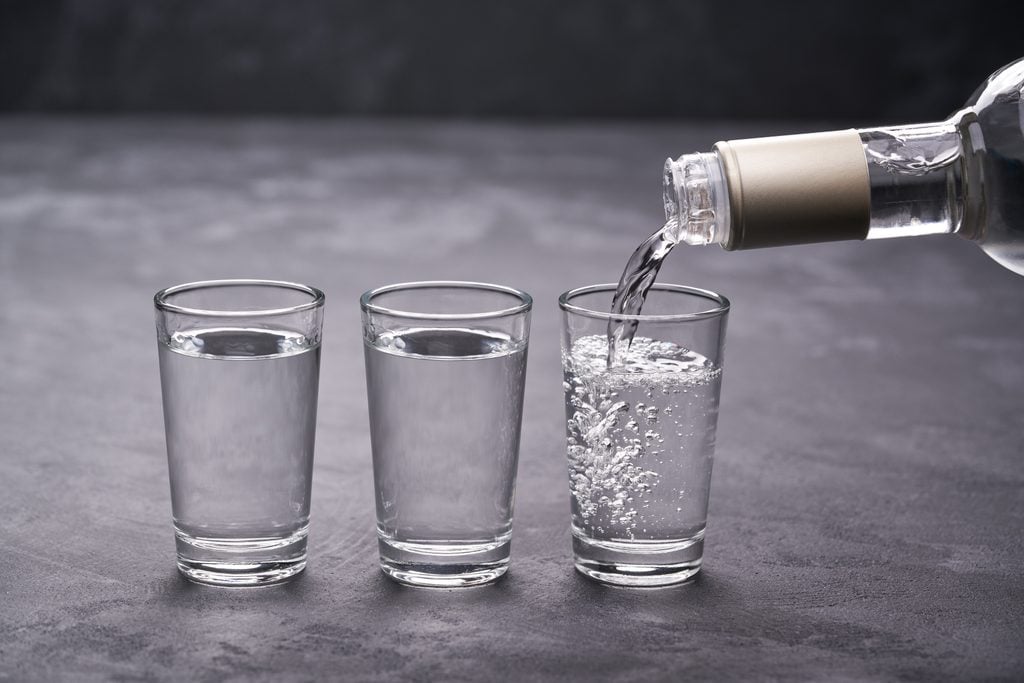 Pouring vodka into the glass on a black background, selective focus
