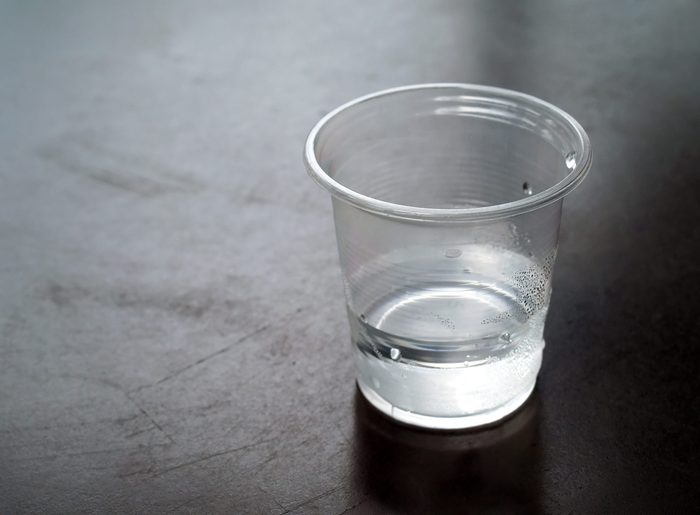 close-up few water in transparent plastic cup with water drops on dark brown metal table with copy space, dark tone image, selective focus