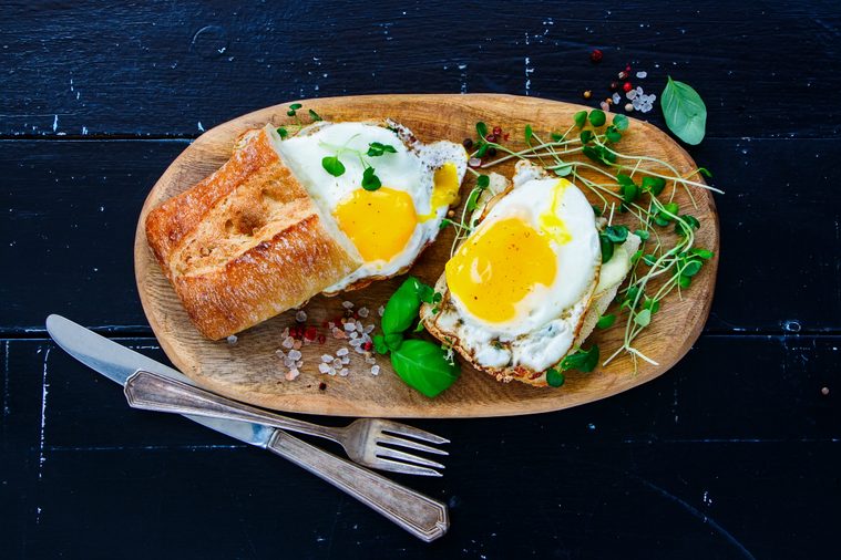 Close up of tasty rural breakfast toast with fried eggs and sprouts on wooden board over black grunge background, top view. Healthy, clean eating, dieting food concept