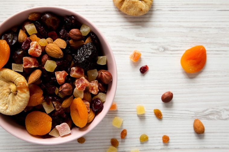 Dried fruits and nut mix in a pink bowl on a white wooden table, top view. Overhead, from above, flat lay. Close-up.