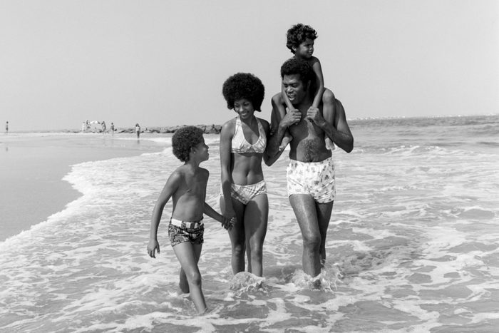 1970s AFRICAN AMERICAN FAMILY MAN FATHER WOMAN MOTHER TWO BOYS SONS WADING IN SURF WALKING ALONG BEACH TOGETHER