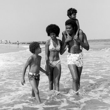 1970s AFRICAN AMERICAN FAMILY MAN FATHER WOMAN MOTHER TWO BOYS SONS WADING IN SURF WALKING ALONG BEACH TOGETHER