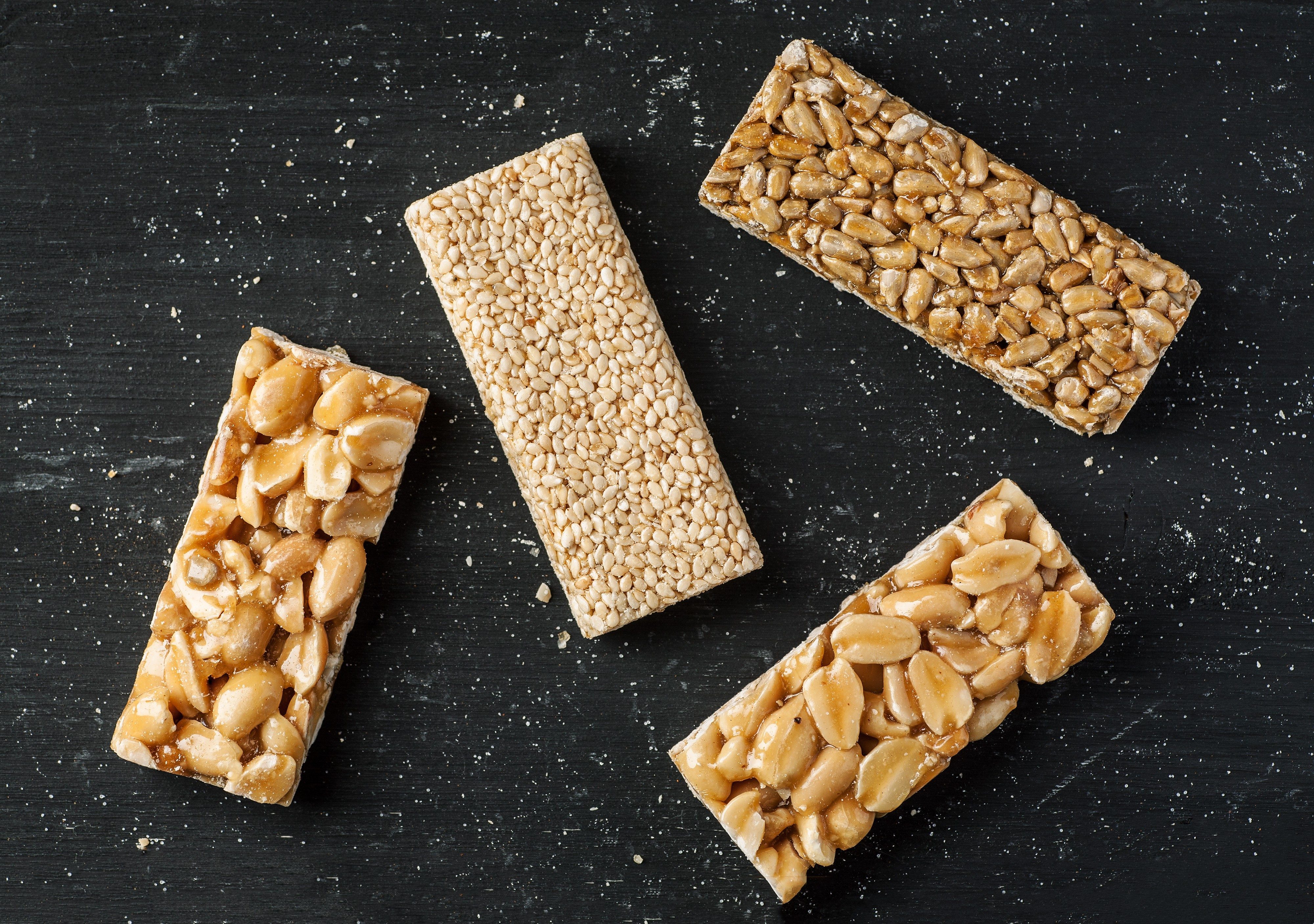 Peanut, sesame and sunflower seed brittle on a black wooden table, top view, flat lay.