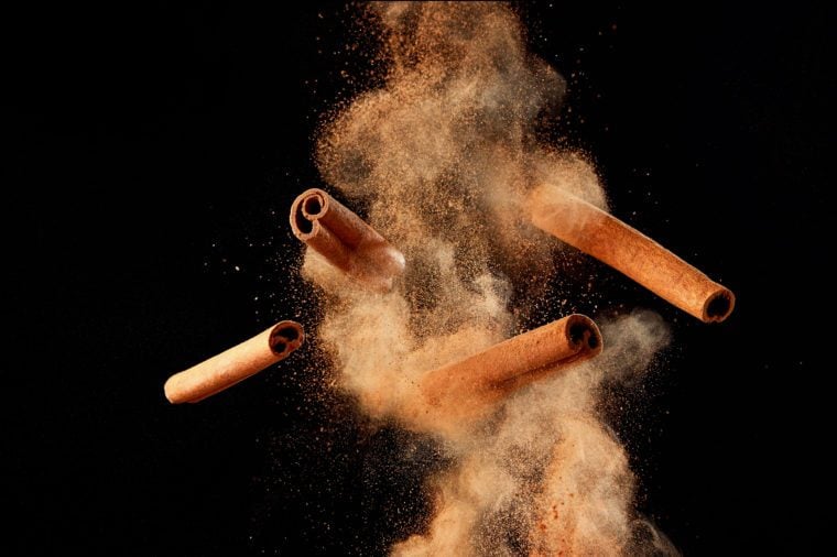 Food explosion with cinnamon sticks and powder, on black background.