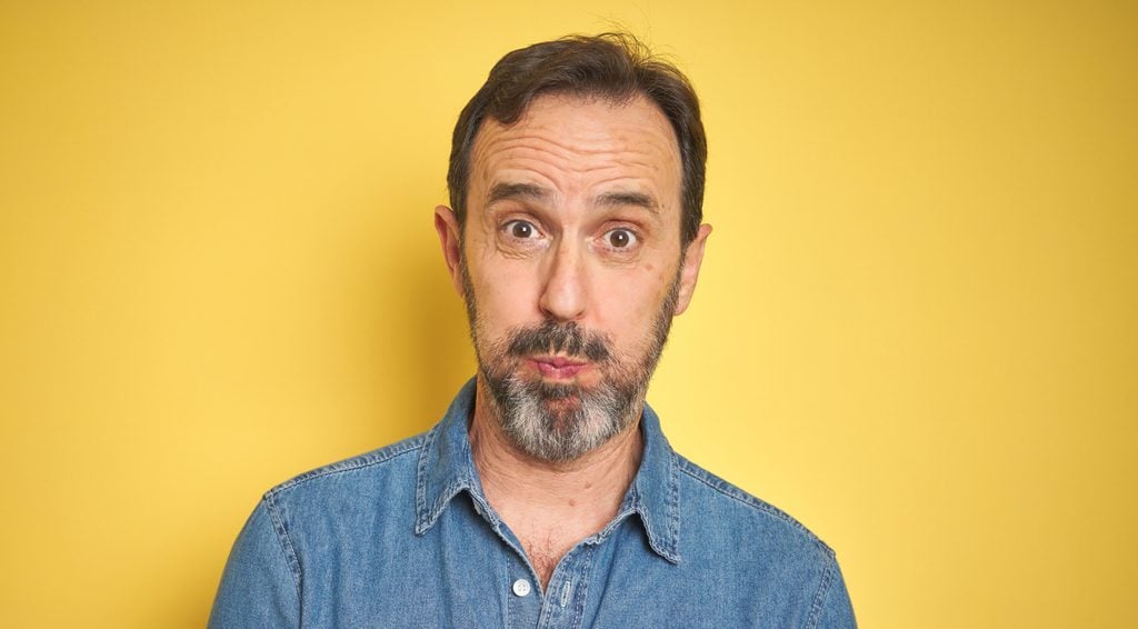 Handsome middle age senior man with grey hair over isolated yellow background puffing cheeks with funny face. Mouth inflated with air, crazy expression.