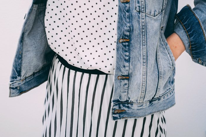 Young adult woman dressed white t-shirt with black peas pattern, striped skirt and denim jacket.