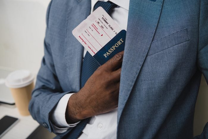 Cropped image of African american man hiding passport and fly ticket into pocket in suit