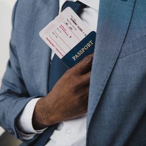 Cropped image of African american man hiding passport and fly ticket into pocket in suit 