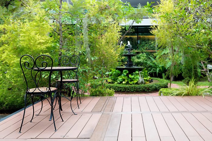 Black chair in wood patio at green garden with fountain in house. Outdoor garden.