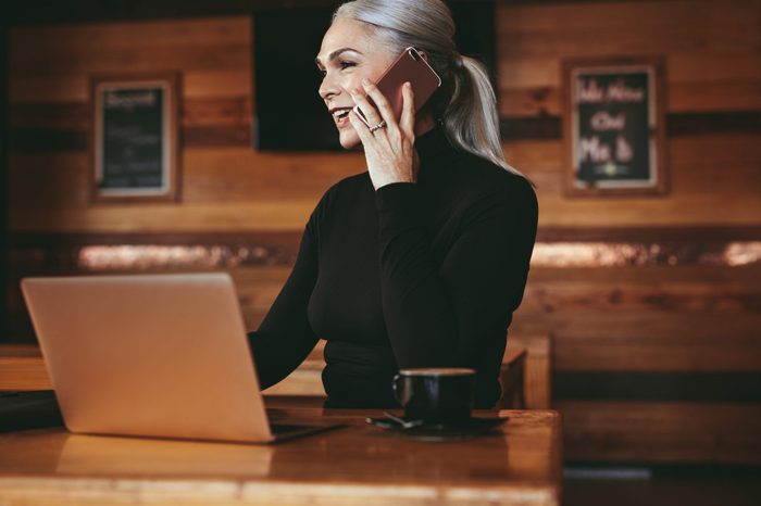 Beautiful senior businesswoman sitting at cafe having telephonic conversation with client. Mature female business professional talking on mobile phone while sitting at coffee shop.