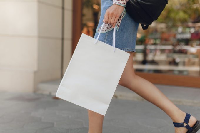 Mockup of white paper shopping bag. Attractive girl doing shopping in shopping mall. Space for your logo or design. Blurred shop window on the background