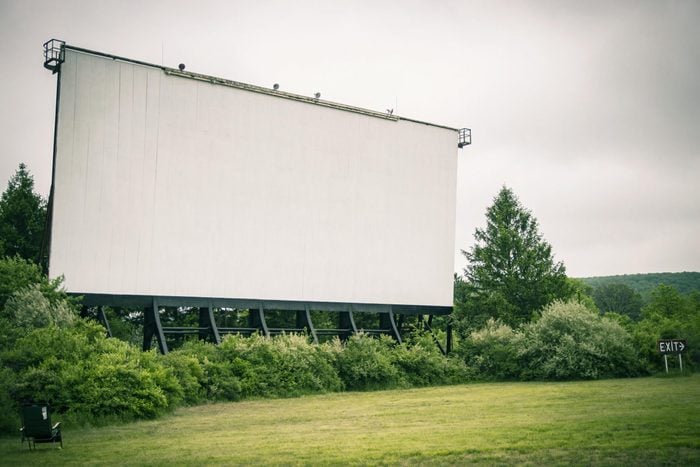The Mahoning Drive-In Theater movie screen stands in the distance; surrounded by grass and wooded overgrowth