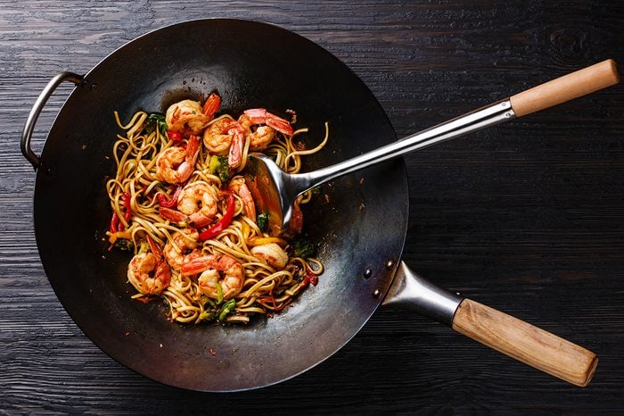 Udon stir-fry noodles with shrimp and vegetables in wok pan on black burned wooden background