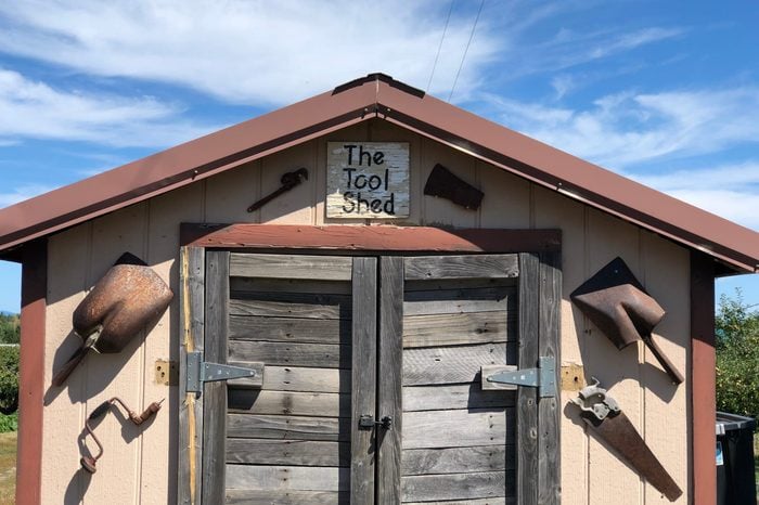 Close view of a tool shed. Old vintage & rusty tools are displayed on the exterior of the building. Beautiful blue skies are visible in the background