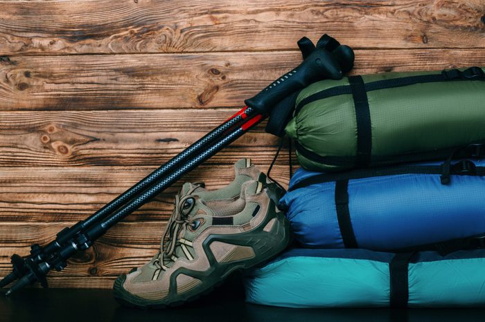 tourist lifestyle with trekking shoes, sleeping bags, tent and trekking poles on wooden background with copy space for text