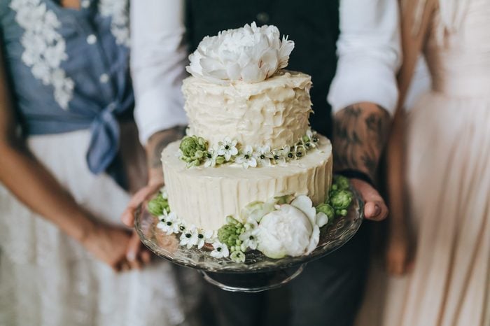 Couple in their wedding clothes holding a white cake decorated with flowers, berries and herbs