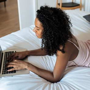 Attractive black woman sitting on bed at home working on the computer