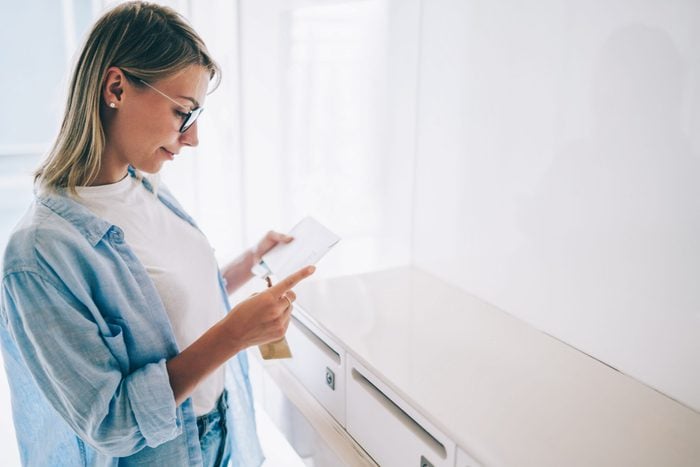 Positive caucasian young woman holding received envelope checking mail from metal letterbox in apartment,pretty caucasian hipster girl in spectacles reading correspondence from postal delivery