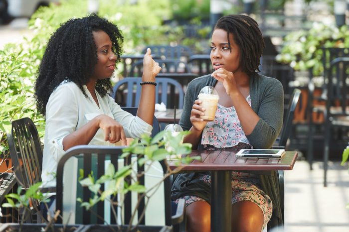 Two pretty Africa-American women drinking cocktails and chatting in cafe