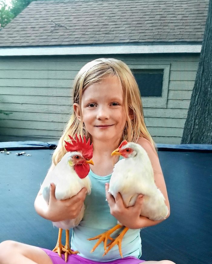 young girl holding a chicken in each arm