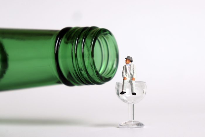 A bottle and a glass. Miniature man sitting on the miniature glass.